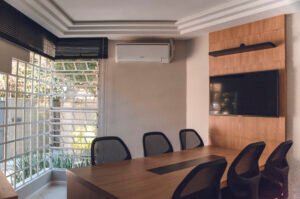 Spacious modern conference room featuring wooden table, chairs, TV, and air conditioning unit.
